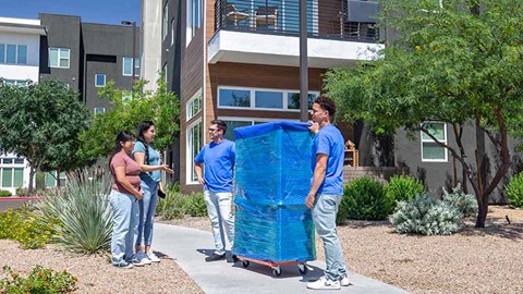 Two moving helpers moving a furniture item on a dolly into an apartment