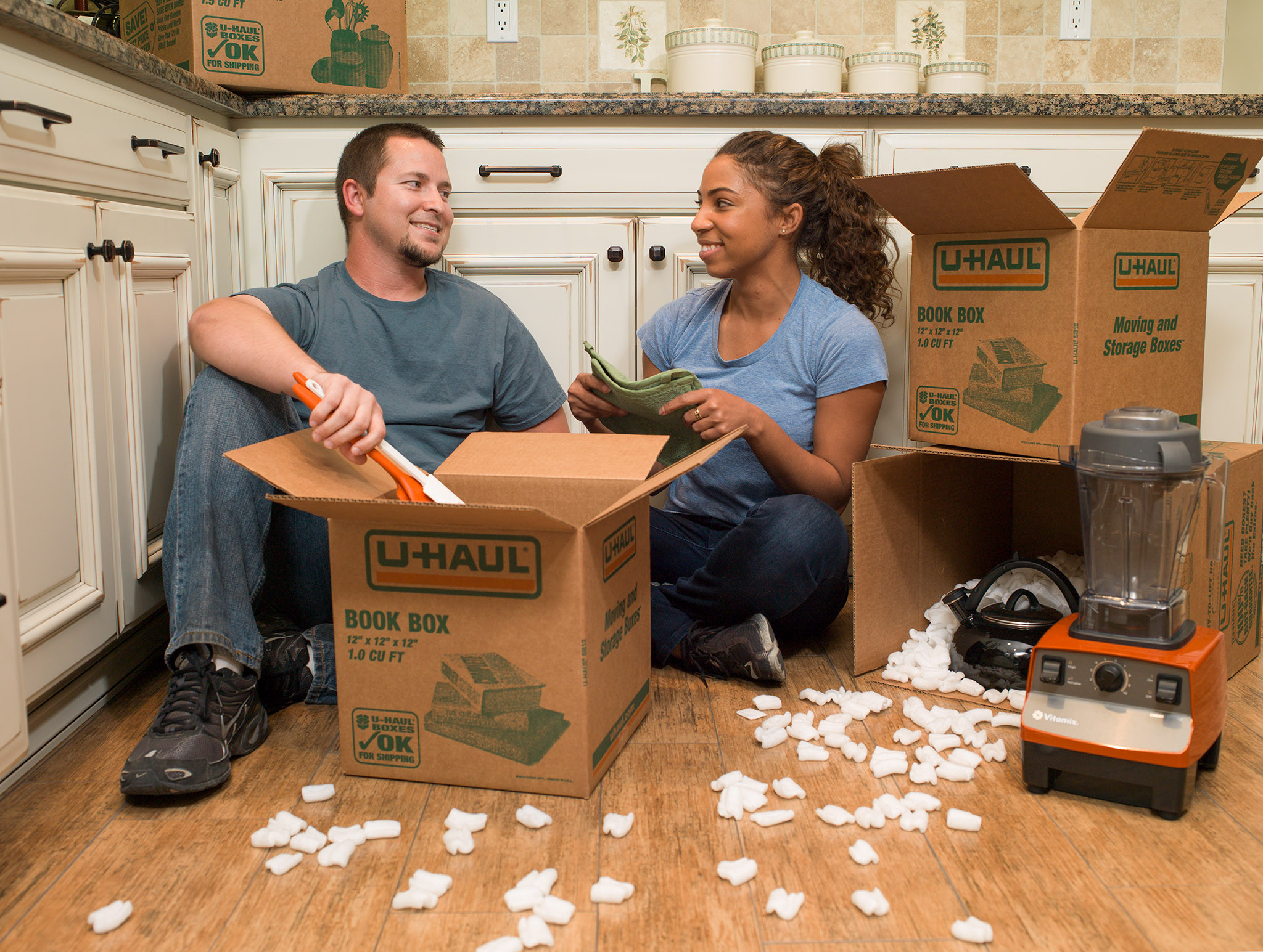 Couple packing up kitchen, using U-Haul boxes.