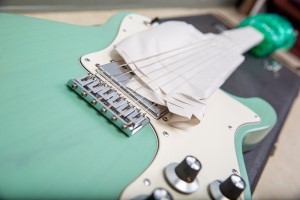 An electric guitar getting prepped for shipping with Packing Paper underneath the strings and Enviro-Bubble around the headstock.