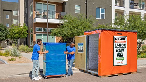 Two Service Providers carefully load a tall furniture piece into a U-Box storage container using a furniture dolly 