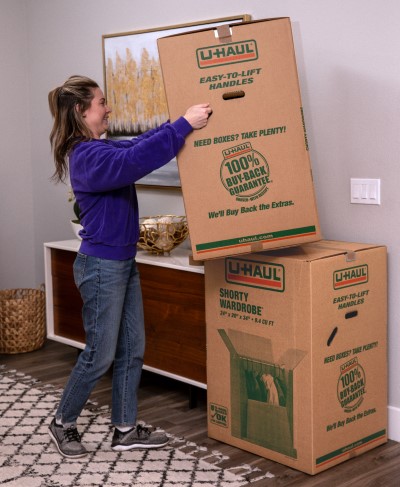 A woman stacking a shorty wardrobe box on top of another wardrobe box.