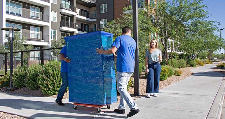 A customer watches two Moving Help Services Providers carefully bring her dresser on a furniture dolly toward her U-Haul truck rental. Once the moving labor providers are finished with the job, and the customer is satisfied, she’ll give her Payment Code to the helpers, which she’ll find using the U-Haul app.