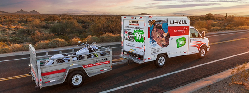 U-Haul truck hauling a full motorcycle trailer at sunset.