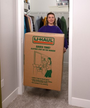 A woman carrying a shorty wardrobe box through a doorway.