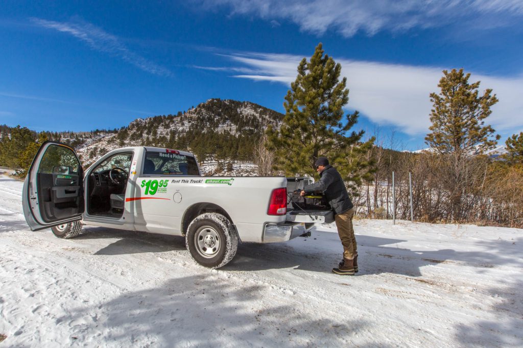 A U-Haul pickup truck parked in the snow. There is a man standing behind the truck and he is loading it up.